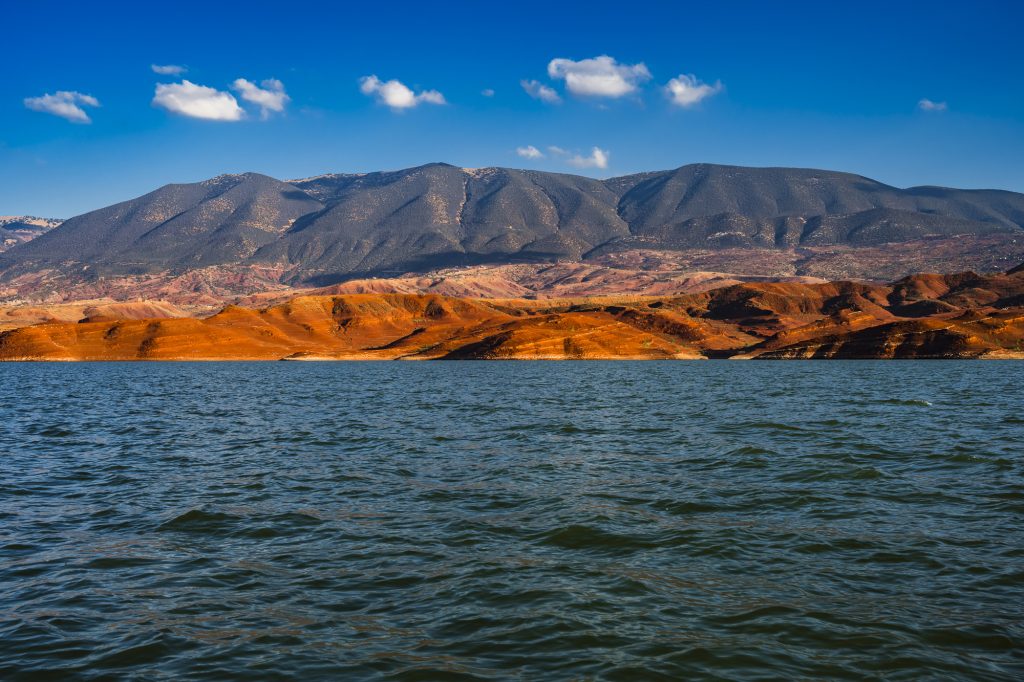 Late afternoon sun over red rocks, the lake and the Atlas Mountains at Bin El Ouidane, Morocco