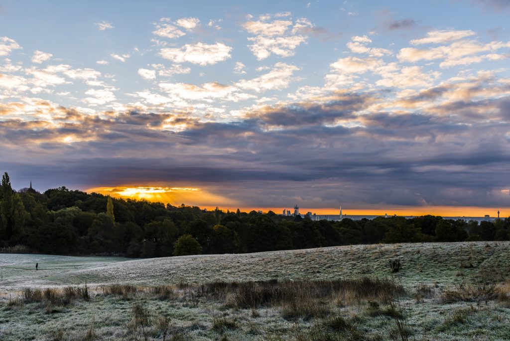 Sunrise and crepuscular rays in autumn over the London skyline from Highgate Church, to Canary Wharf, via the The Shard to the BT Tower, taken from Hampstead Heath, London
