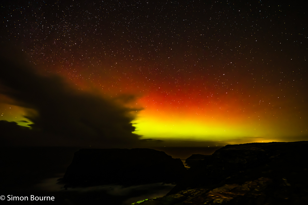 Northern Lights (Aurora Borealis) and winter stars over Tintagel Island from Glebe Cliff, Tintagel, Cornwall, UK