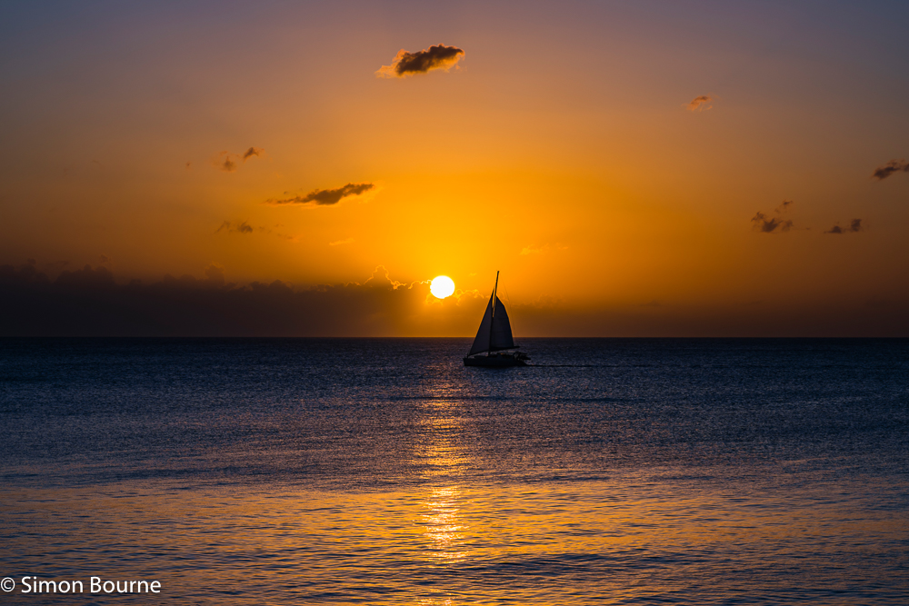 Tropical sunset and orange skies with a passing yacht on the Caribbean Sea at Prospect Bay, Barbados