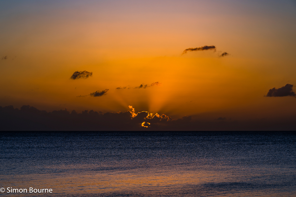 Tropical sunset, orange skies and crepuscular rays, over the Caribbean Sea at Prospect Bay, Barbados