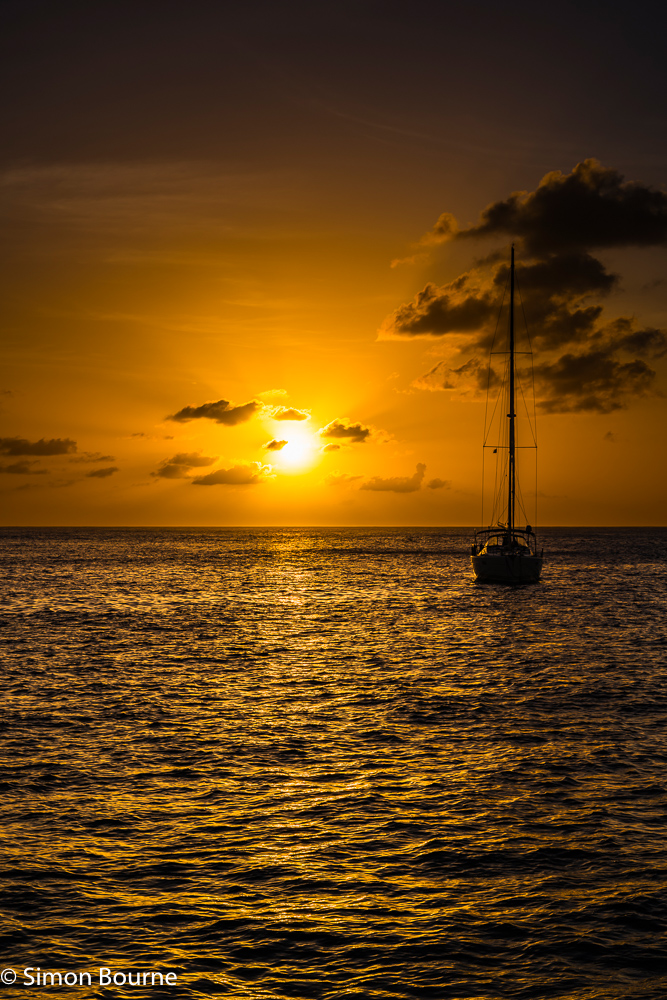 Sunset and reflections over the sea with crepuscular rays and a moored yacht, just off Young Island, at the southern tip of the tropical Caribbean island of St Vincent and the Grenadines