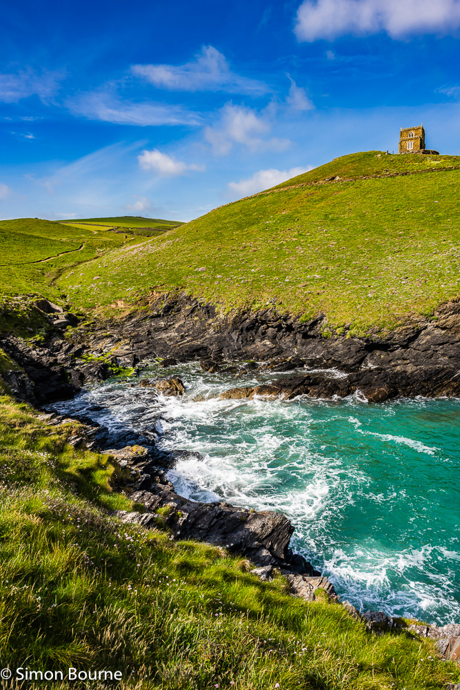 Spring flowers on the cliffs and surf in the sea near Doyden Castle at Port Quin harbour, Cornwall